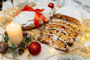 Fototapeta na wymiar Traditional German Christmas stollen made of dried fruits and nuts, sprinkled with powdered sugar on the background of a Christmas decor with candles. A festive treat.