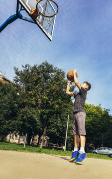 Cute Boy In Gray T Shirt Plays Basketball On City Playground.