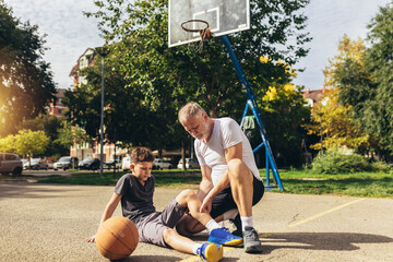 Father helping boy with legs trauma after playing basketball. Sports Injury.