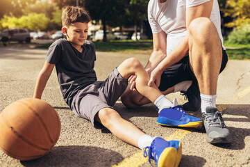 Father helping boy with knee trauma after playing basketball. Sports Injury. - Powered by Adobe