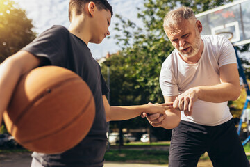Father helping boy with fingers trauma after playing basketball. Sports Injury.