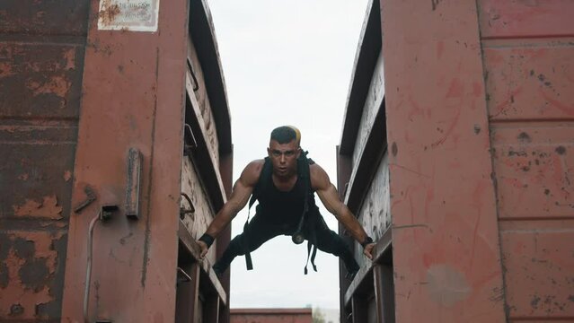Young muscular man with balloon drager on his back is training at railway yard and doing push-ups resting his hands on freight wagons