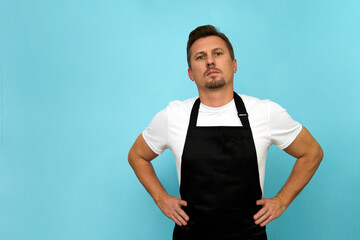Young barista in black apron and white t-shirt on blue background