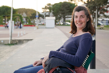 smile middle aged brunette woman siting bench in city