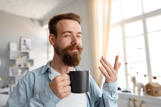 Young bearded man smiling and drinking coffee at home