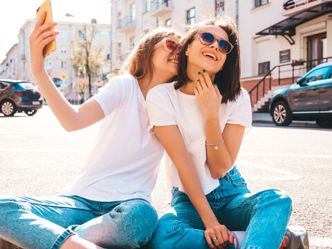 Portrait of two young beautiful smiling hipster female in trendy summer white t-shirt clothes.Sexy carefree women posing on street background. Positive models having fun, taking selfie photos