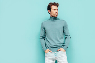 Portrait of handsome confident  model. Sexy stylish man dressed in  sweater and jeans. Fashion hipster male with curly hairstyle posing near blue wall in studio. Isolated - obrazy, fototapety, plakaty