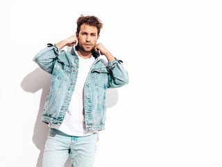 Portrait of handsome confident stylish hipster lambersexual model. Sexy man dressed in jeans jacket. Fashion male isolated on white wall in studio
