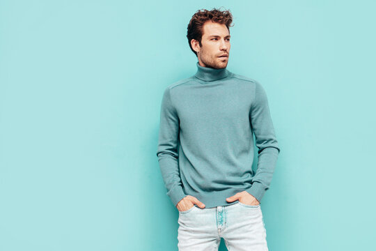 Portrait of handsome confident  model. Sexy stylish man dressed in  sweater and jeans. Fashion hipster male with curly hairstyle posing near blue wall in studio. Isolated