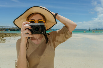 woman wearing sunglasses standing on the beach take a photo by digital camera with sunny day