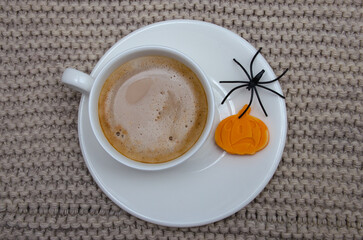 Morning fragrant coffee with candies in the form of pumpkins, the atmosphere of the Halloween holiday. Close-up of a porcelain coffee cup with fragrant coffee and delicious chocolate figure candy