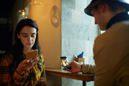 Modern young couple using their smartphones while sitting together in cafe in front of each other
