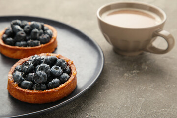 Blueberry tartlets on dark plate with cup of coffee. Homemade tarts with black berries.
