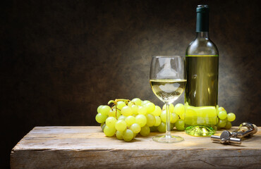 White wine glass with bottle, corkscrew and bunch of grapes on old wooden table, space for text.