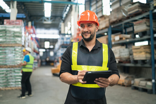 Professional manager man employee smile using tablet check stock working at warehouse. Worker wearing high visibility clothing and a hard hat, helmet checking and count up goods or boxes for delivery