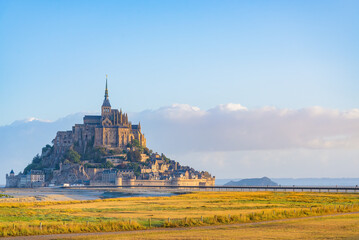 The famous "Mont Saint Michel", Normandy, France. Yellow field on the foreground. Blue sky and big cloud on the background.