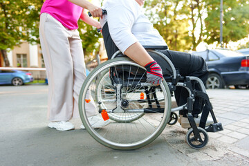 Obraz premium Young female caregiver pushing wheelchair with female person with disability across city street