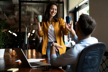 Colleagues laughing in office. Businesswoman and businessman drinking coffee
