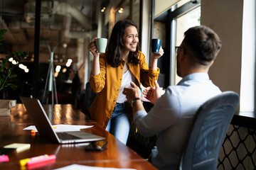 Colleagues laughing in office. Businesswoman and businessman drinking coffee