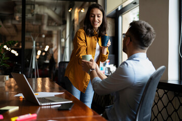 Colleagues laughing in office. Businesswoman and businessman drinking coffee