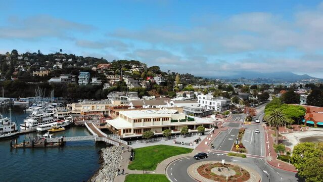 Ascending aerial shot showing beautiful City of Tiburon, California with cars in roundabout beside Harbor during sunlight and blue sky