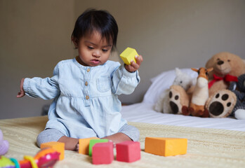 Down syndrome, daycare and baby on the bed with toys, playing with color shapes and blocks. Child...