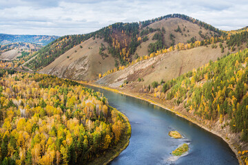 A small river flows in the mountains, overgrown with forests. View from the mountain to a beautiful autumn landscape