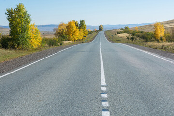The asphalt road runs through the steppe and goes far into the mountains. Autumn