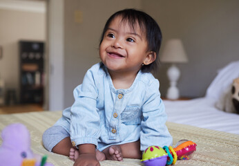 Down Syndrome, smile and happy baby relax on bed having fun, play with toys and enjoy happiness at...