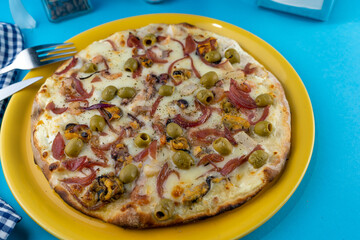 Pizza with mussels and green olives. Food in a yellow plate on a blue background. Menu. Homemade pastries. Meal with meat. Food on the table