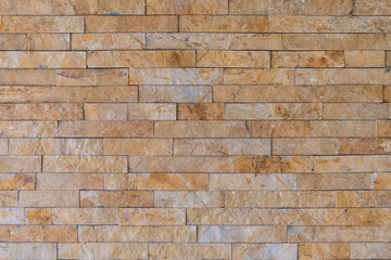 Brick wall facade background. Wall with decorative beige embossed cladding of narrow granite tiles.