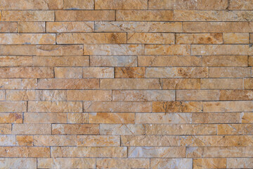 Fototapeta premium Brick wall facade background. Wall with decorative beige embossed cladding of narrow granite tiles.