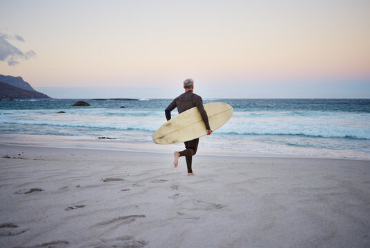 Surf at the beach, man and running to ocean with surfboard for the waves, fitness and adventure. Mature surfer at sunrise, in wet suit and to enjoy the sea, travel and summer on an island.