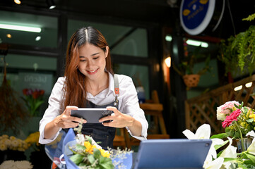 Pretty Asian female florist taking photo of finished flowers bouquet for shop's social media.