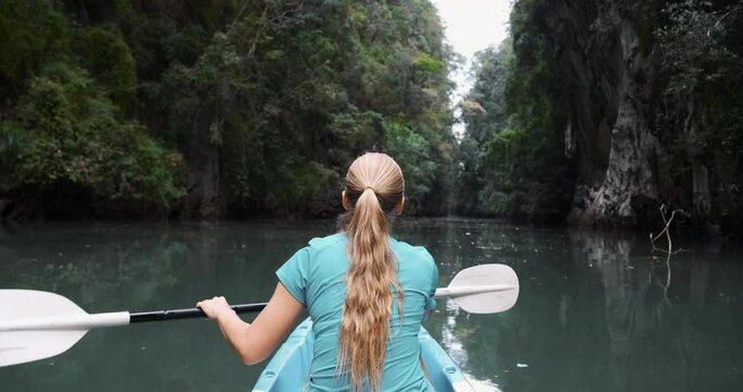 Woman tourist rows paddle on kayak swimming on tropical river surrounded by rocks. Vacations and active holidays. Kayaking sport, canoeing