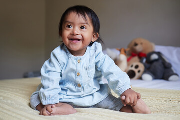 Baby, down syndrome and special needs child happy with a smile sitting on a bed to relax, be...