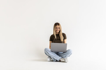 Portrait of a woman holding laptop computer while sitting on a floor over white background