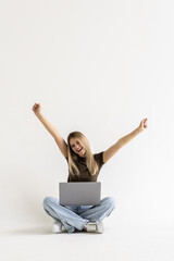 Young woman sitting with laptop with win gesture on white background