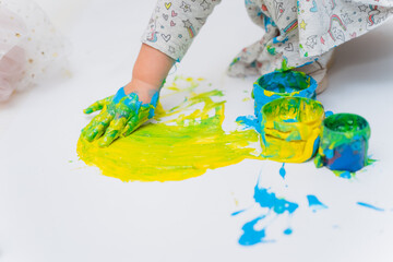 A small child draws with his palm on a sheet. The kid's hand in yellow gouache is painting on the...