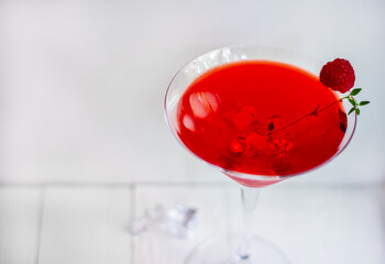 Close-up of red alcohol cocktail with raspberries and thyme on the white wood table.