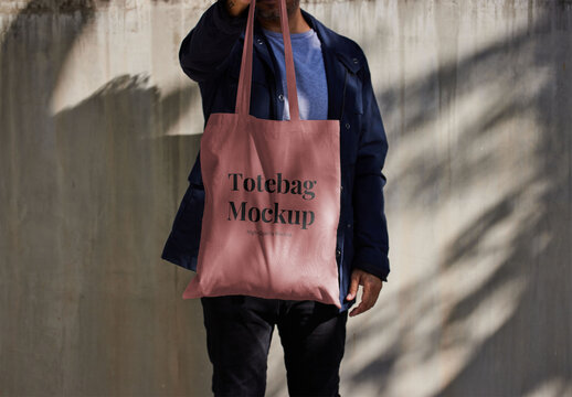 Man Holding Tote Bag Mockup On Concrete Wall
