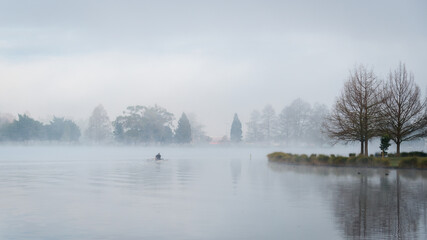Man rowing a boat on the lake, heavy fog drifting on the lake.