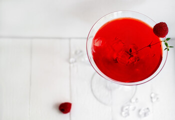 Close-up of red alcohol cocktail with raspberries and thyme on the white wood table.
