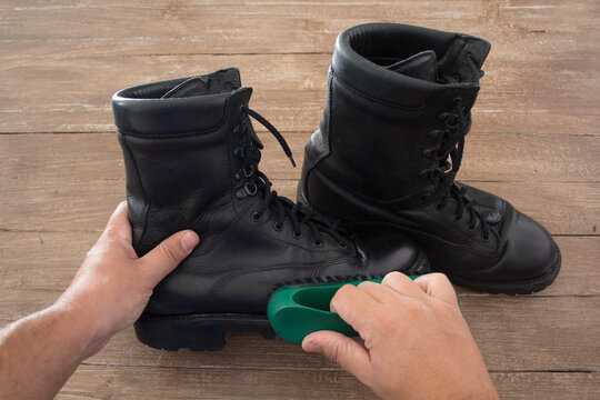 Image of the hands of a man who polishes a pair of military boots with a shoe brush.
