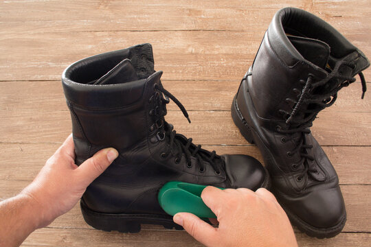 Image of the hands of a man who polishes a pair of military boots with a shoe brush.
