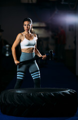 Fototapeta na wymiar Portrait of fit beautiful muscular woman holding big hammer posing near huge tire wheel.