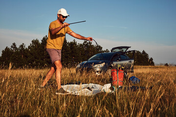 Man camping in nature, unpacking and packing small tent outdoors, recreation and hobbies.