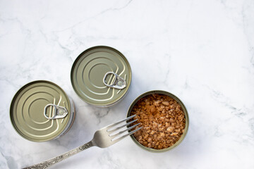 Open tin can with chopped tuna in oil on white marble kitchen table. Canned fish in a tin can. Top view, copy space