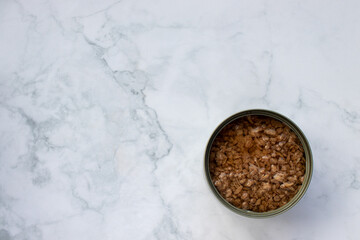 Open tin can with chopped tuna in oil on white marble kitchen table. Canned fish in a tin can. Top view, copy space