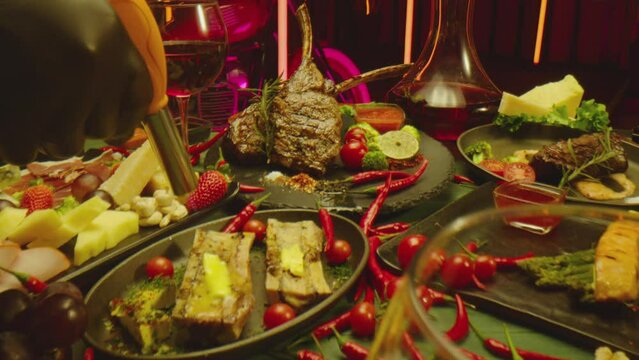 Camera moving across table , served with wine , steak , various types of cheese vegetables hot red peppers . Tasty expensive food inside restaurant . Shot on ARRI ALEXA Cinema Camera with Laowa lense